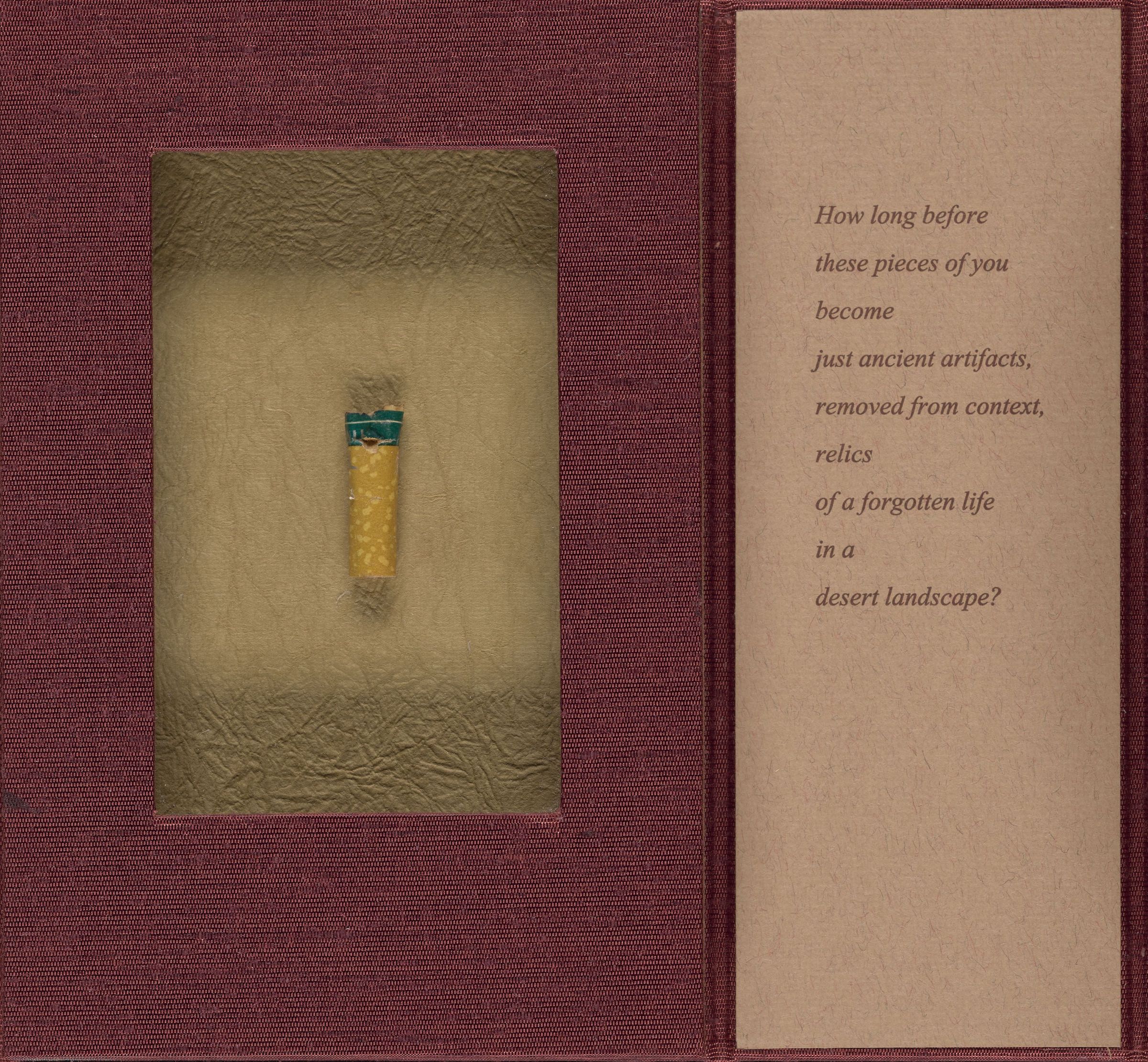 Photo of dark red artist book featuring cigarette butt and text on tan paper